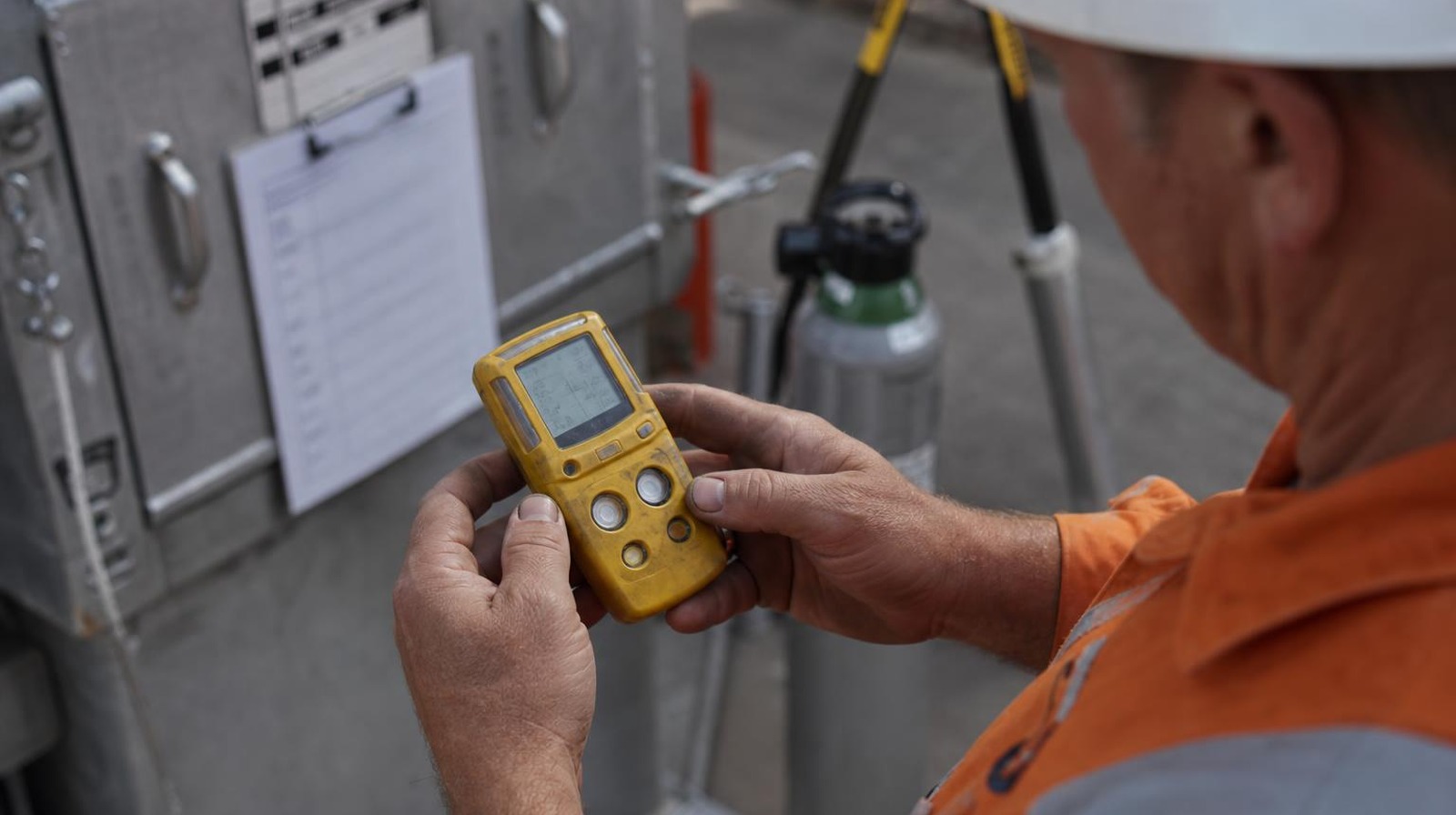 Trainer running a bump test on a yellow four-gas atmospheric monitor next to a confined space entry permit clipboard and calibration gas cylinder at a Perth training yard.
